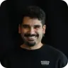 Smiling man with dark hair and beard on a black background.