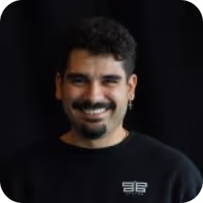 Person with a mustache smiling in front of a dark background.
